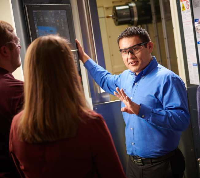 NCMT CNC trainer delivering hands-on machine operation training to engineers at control panel in UK technology centre.