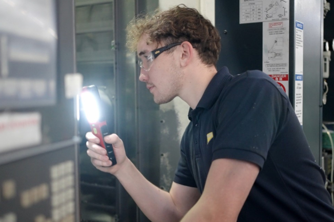 NCMT field service engineer inspecting CNC machine cabinet using diagnostic tools during repair visit.