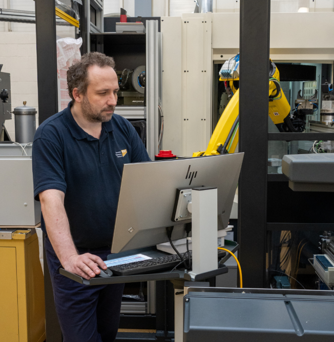 men-with-machine NCMT automation engineer programming robotic machining cell using industrial control workstation in Coventry Technology Centre.